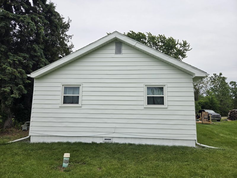 Exterior house painting, white siding and trim. Gable end wall with two small windows, and white gutters.